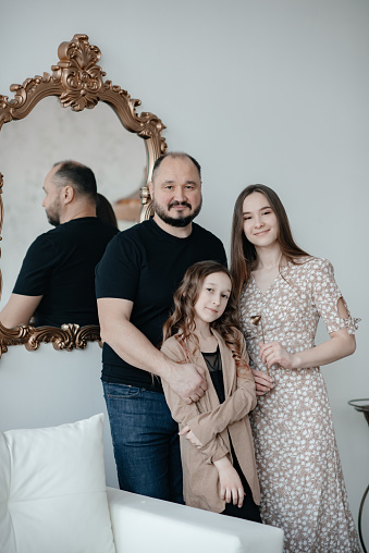 A beautiful young girl with long hair in a light summer dress poses at home with her father and sister. Holiday concept. Family photo. Father with two daughters.