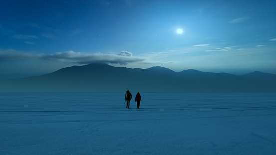 The two people walking through the night snow field on the mountain background