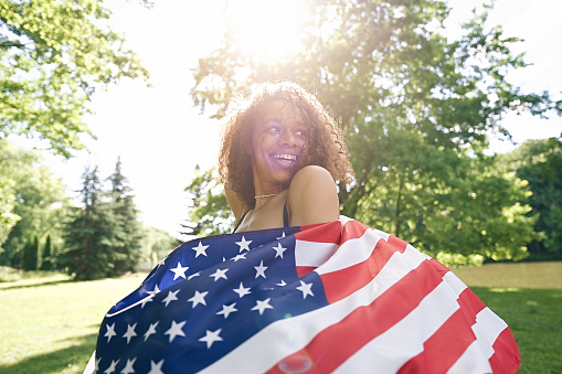 Young African american woman is waving American flag on top of at nature background. USA resident, US citizen. Immigration concept