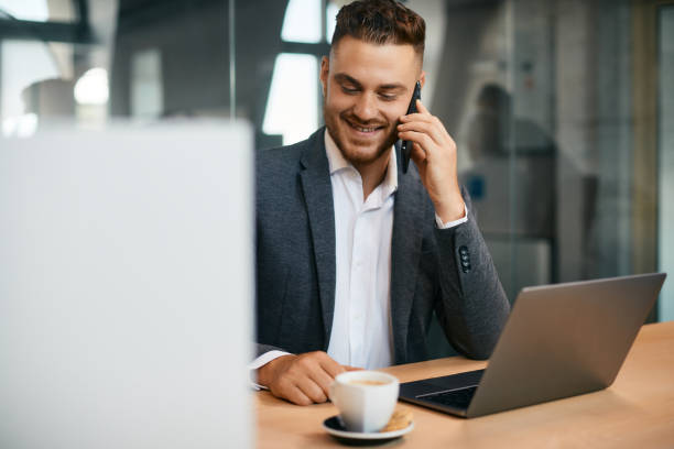 istock Happy businessman making a phone call while working on laptop in the office. 1406775866
