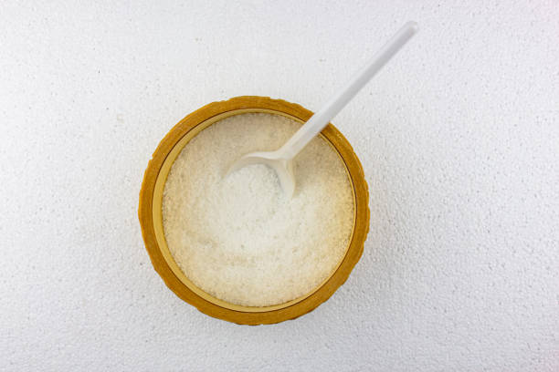 The Salt in a wooden bowl with a white spoon on a white background. Table salt on the kitchen table.