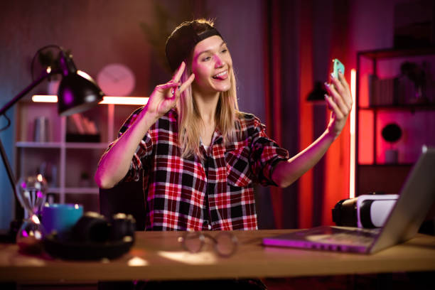 istock Pretty blond woman in cap taking selfie on smartphone while sitting at home office. 1406778428