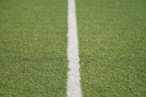 Photography of green synthetic artificial grass soccer sports field with white stripe (line) in the middle. Sportive theme. Close up