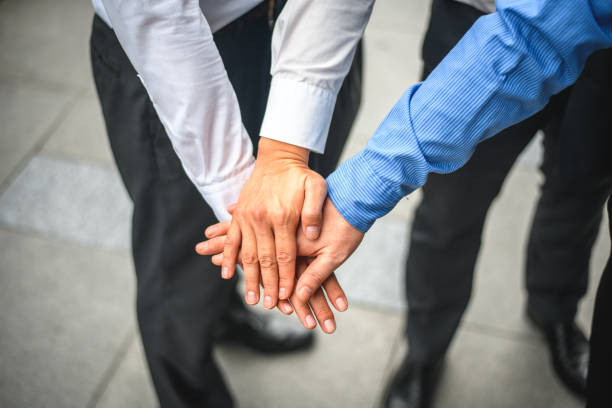 High angle view of three male hands, one on top of the other. The hands are from three businessmen that are wearing formal clothes.