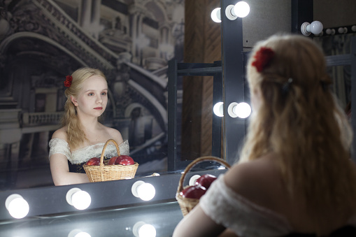 Young blonde woman in vintage dress looking through the mirror in dressing room