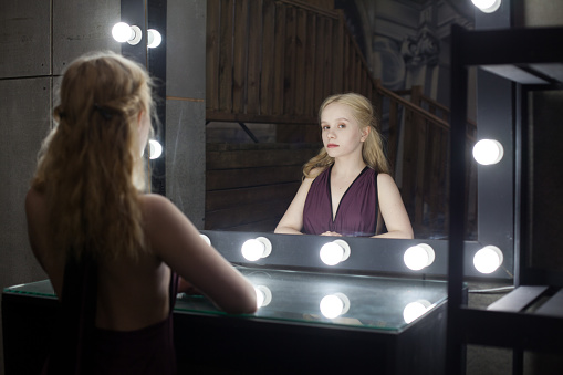 Beautiful young adult woman blonde looking at her reflection in a dressing room mirror