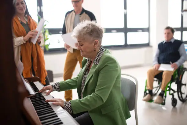 Photo of Senior woman playing at piano in choir rehearsal.