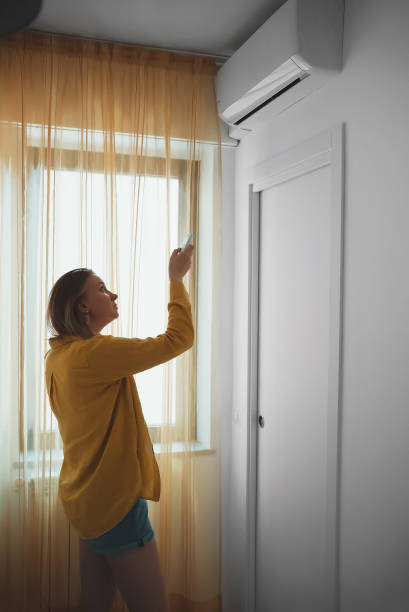 istock Woman holding remote control aimed at the air conditioner. 1406789806