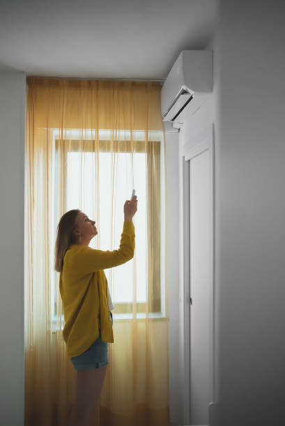 istock Woman holding remote control aimed at the air conditioner. 1406789822