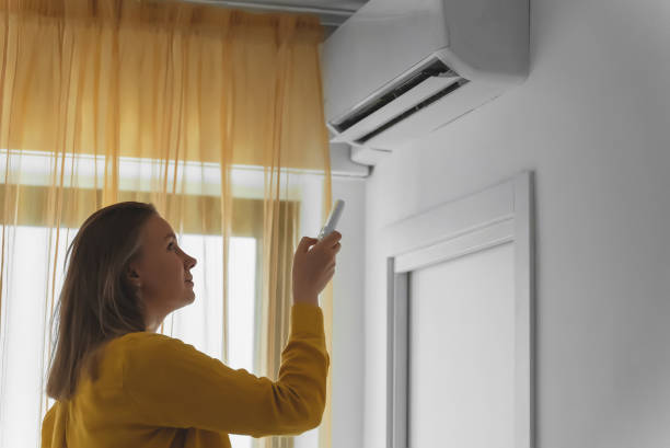 istock Woman holding remote control aimed at the air conditioner. 1406789837