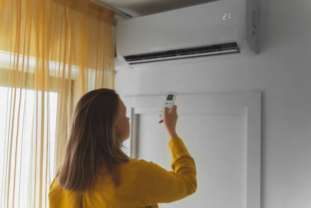 istock Woman holding remote control aimed at the air conditioner. 1406789839