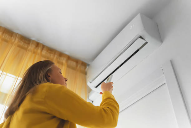 istock Woman holding remote control aimed at the air conditioner. 1406789856