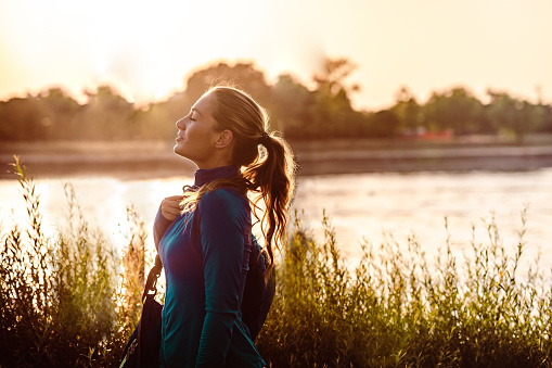 Side view on young woman in sportswear walking by the river and enjoying the sun