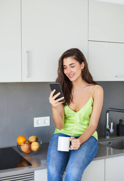 istock A cheerful woman with a smartphone sits in the kitchen while drinking coffee. 1406791222