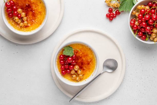 creme brulee, cream brulee, burnt cream with currant in ramekins. traditional french vanilla cream dessert with caramelised sugar on top. homemade dessert with berries. top view. selective focus. - custard creme brulee french cuisine crema catalana imagens e fotografias de stock