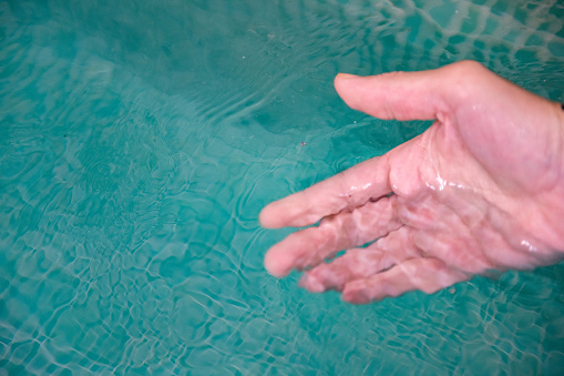 This is a color photograph of a the hand of a caucasian man in his early 40s testing the water  in a hot tub.