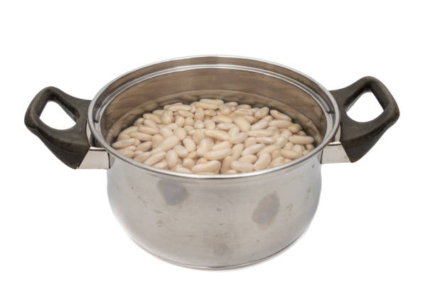 ステンレス製の鍋に水に浸したネイビービーンズ。白い背景に分離されています。 - variation bean beige cannellini bean ストックフォトと画像