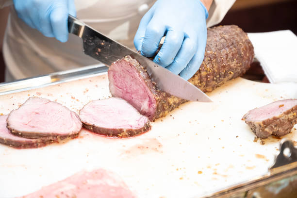 The hand of the cook who is cutting the roasted beef