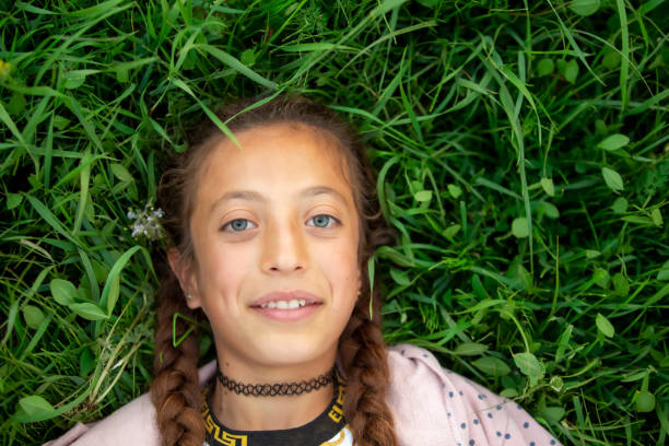 The girl is lying on the grass.  The girl has blond hair and blue eyes.  The girl is white skinned.