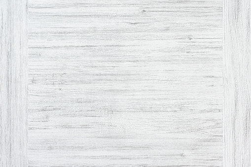 White wood background. Rough white painted old wooden board. A wood grain pattern featuring even grains of wood running horizontally across the image. The board has few cracks and knots.