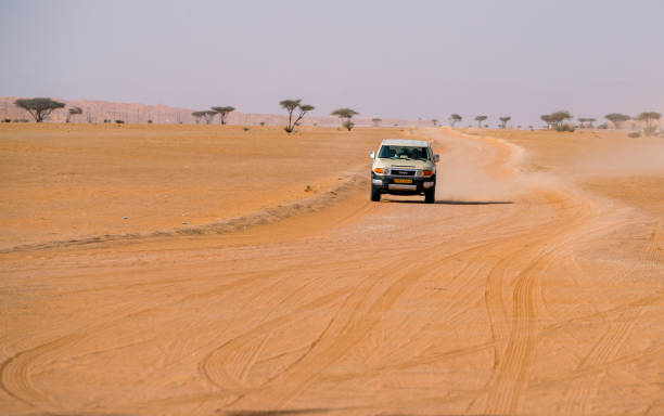 Wahiba Sands, Oman - 04.03.2018: Frontal shot of white Toyota offroad driving on a dirt road through Arabian desert with lots of dust and heat haze