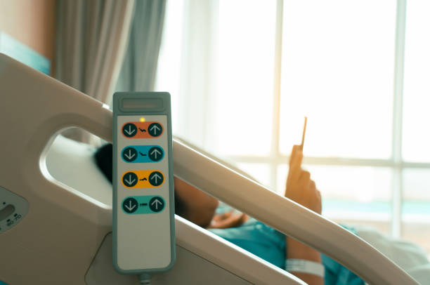 Hospital bed remote control hanging on the bed rail with woman patient on bed in hospital room. stock photo
