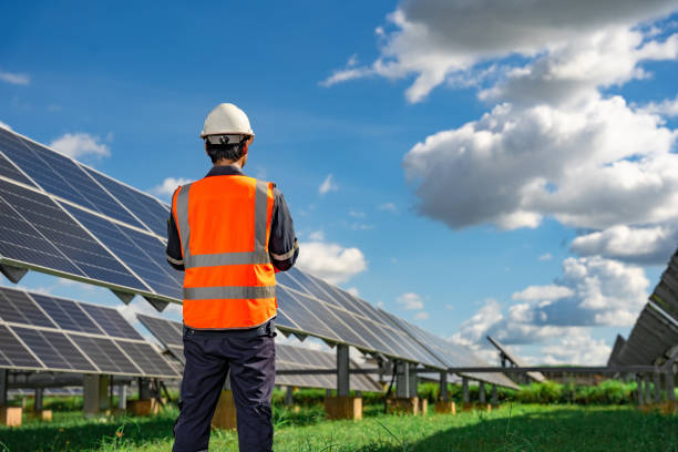 istock Technician dressed in blue uniform and in an orange reflective vest and wearing a safety helmet stands facing a solar panel at solar power plant, Photovoltaic module idea for clean energy production 1406826152