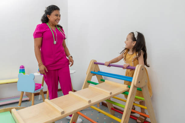 niña escalando un juego en el consultorio pediátrico, mientras el pediatra la observa - occupational therapy fotografías e imágenes de stock
