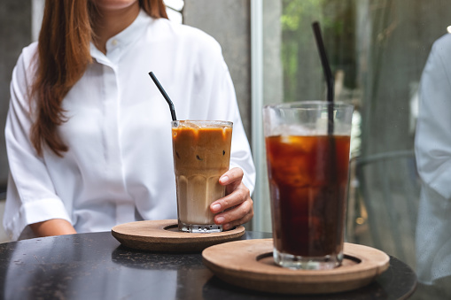 Closeup image of a woman holding a cup of iced coffee on the table in cafe