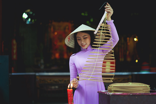 Vietnamese woman in traditional dress praying with incense stick in the burning pot of the Chinese temple, Ho Chi Minh Vietnam