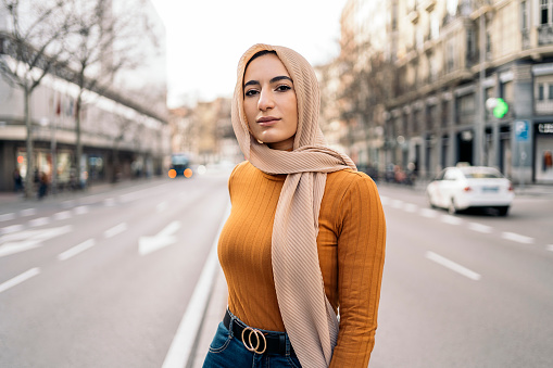 Pretty young muslim woman wearing pink head scarf smiling and looking to at camera in the street.