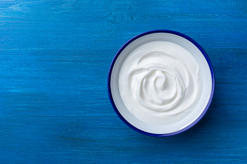 Greek yogurt in bowl on blue wooden table top view.