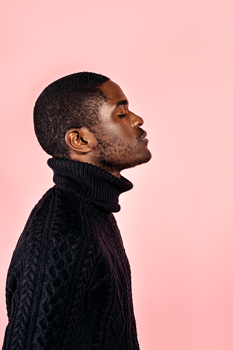 Stock photo of young black man with closed eyes posing in studio shot against pink background.