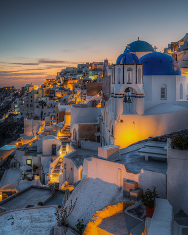 Scenic panoramic view of Oia village at sunset with the iconic blue domed church in the foreground, Santorini, Greece