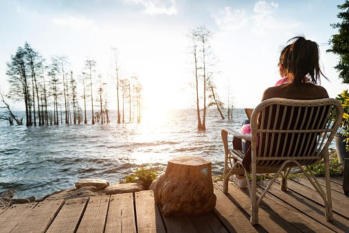 Woman sitting on chair and reading book by the lake.