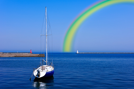 Rainbow over the lighthouse and yacht against clear sky.