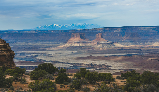 Aerial view overlooking sandstone buttes, plain desert and mountain ranges in Canyonlands National Park, Utah, USA.