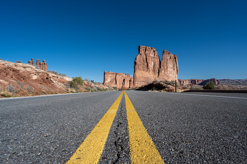 Straight desert road with yellow dividing lines seen at Arches National Park in the Southwest USA a hot summer morning.