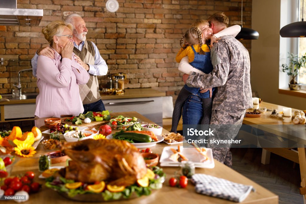 Homecoming of a military father on Thanksgiving! Happy mother and daughter embracing military father in grandparent's kitchen who came back from a war on Thanksgiving day. Thanksgiving - Holiday Stock Photo