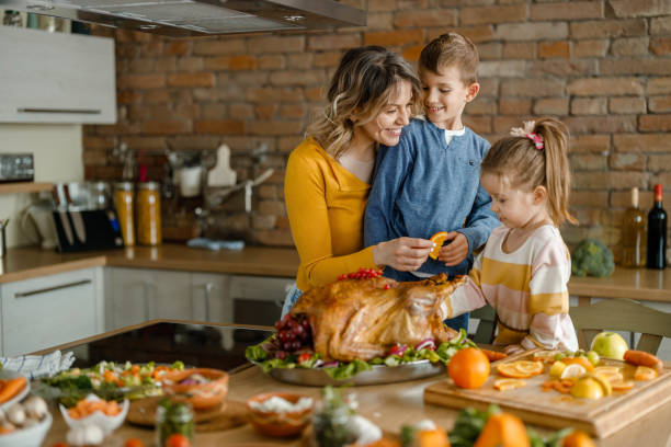 Happy single mother and her kids decorating Thanksgiving turkey. Happy single mother and her small kids decorating turkey on Thanksgiving day in the kitchen. family dinners and cooking stock pictures, royalty-free photos & images