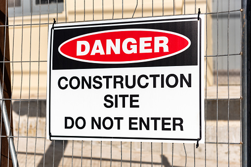 A 'DANGER CONSTRUCTION SITE, DO NOT ENTER' sign mounted on a wire fence in front of a building site