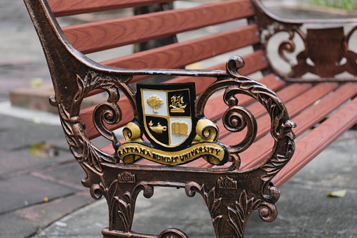 Bangkok, Thailand - March 22 2022: A retro-style bench at the campus of Rattana Bundit University, with a cast-iron university's coat of arms