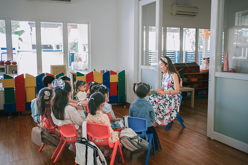 Asian Montessori preschool students enjoy listening to teacher story telling in classroom