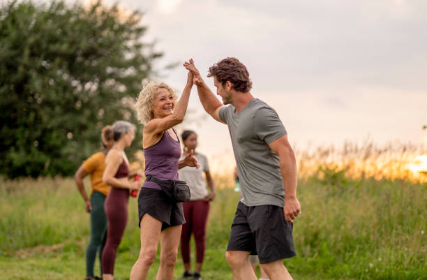 Hi-Five After a Successful Run A mature woman and young man, hi-five each other after a successful group run together.  They are each dressed comfortably in athletic wear and their peers can be seen in the background holding water bottles as they hydrate and cool down. carpet runner stock pictures, royalty-free photos & images