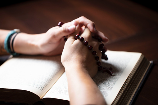 Christian woman with Bible praying with hands crossed keeping rosary.