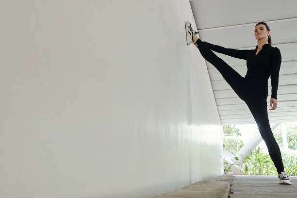 Portrait of young athletic woman in black standing on vertical split leaning on wall during training outdoors