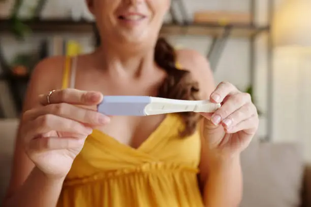 Close-up of happy woman looking at positive pregnancy test in her hands