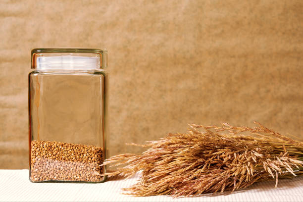 Kitchen table with dry brown buckwheat grain in the transparent jar. Rural dry food grain and cooking background template with copy space
