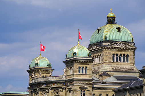 Federal Palace of Switzerland with waving Swiss flags at City of Bern, capital of Switzerland, on a blue cloudy summer day. Photo taken June 16th, 2022, Bern, Switzerland.