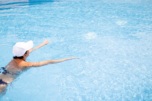 Young woman in white cap swimming in a pool with blue clear water. Summer holidays concept.